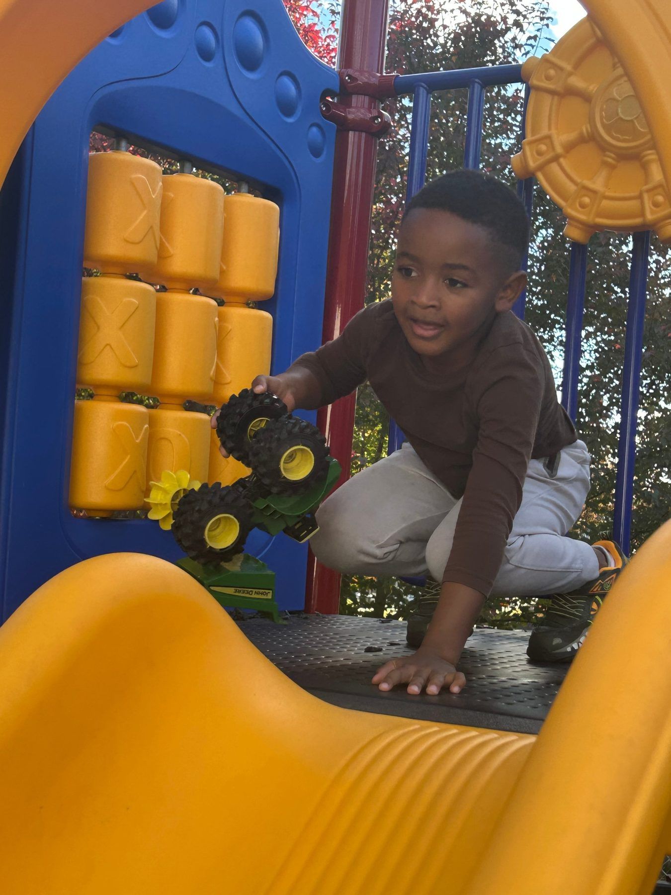 A school-age boy climbing on the playground with a toy tractor