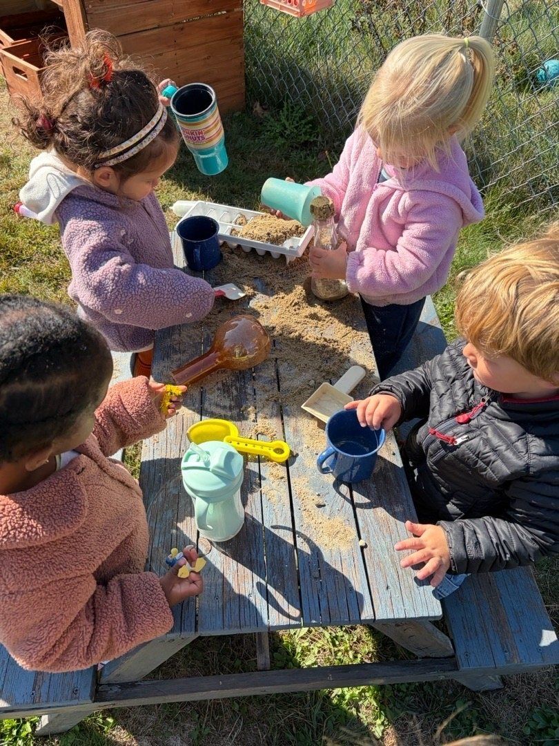 Four kids scooping and pouring at an outdoor sand table