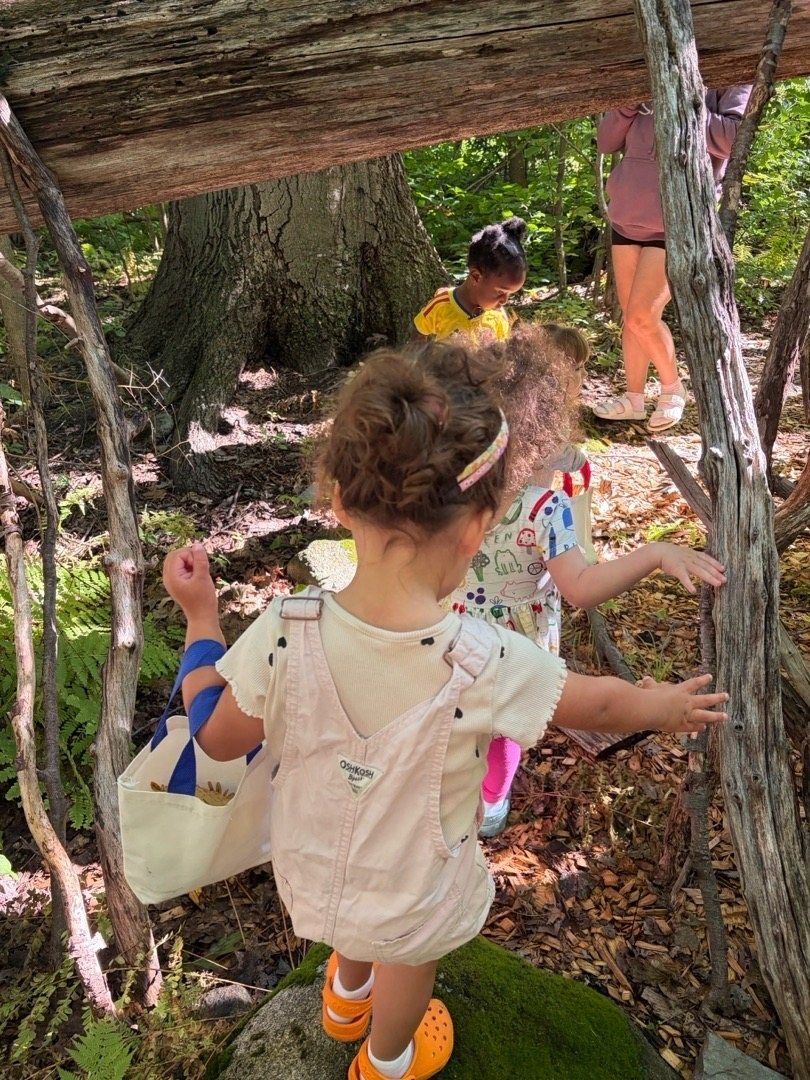 Kids exploring a stick fort in the woods with a teacher nearby